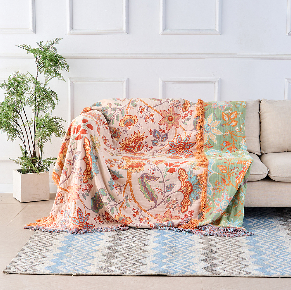A floral blanket with orange and blue flowers on a cream background, draped over the arm of a sofa, with a decorative fringe.